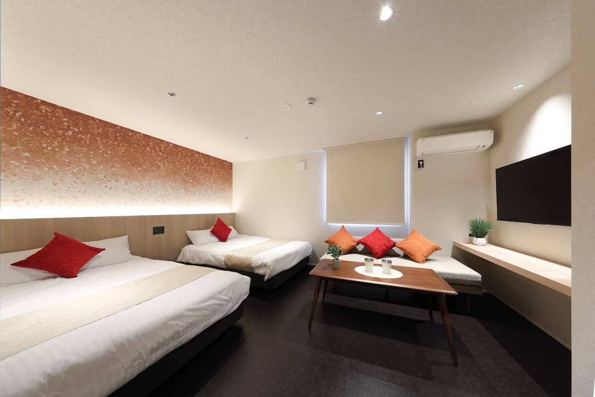 Una habitación de hotel con dos camas, una mesita, un televisor y una ventana.