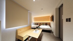 Habitación de hotel con sofá, una mesita con dos tazas, cama con almohadas y televisión montada en la pared.