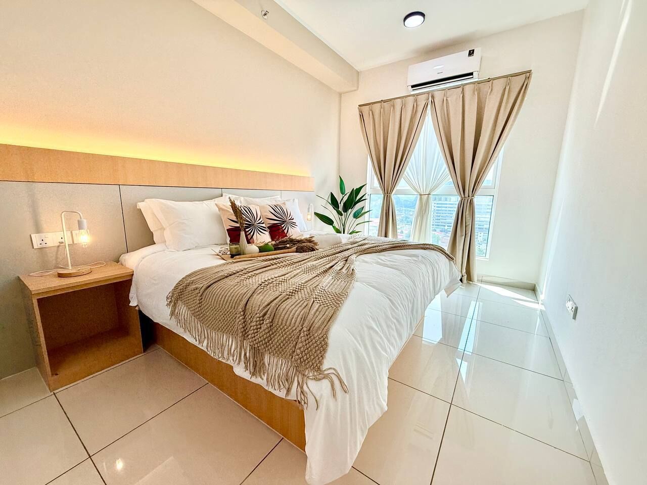 Een moderne slaapkamer met een groot bed, nachtkastjes, een raam met gordijnen en een aan het plafond gemonteerde airconditioner.