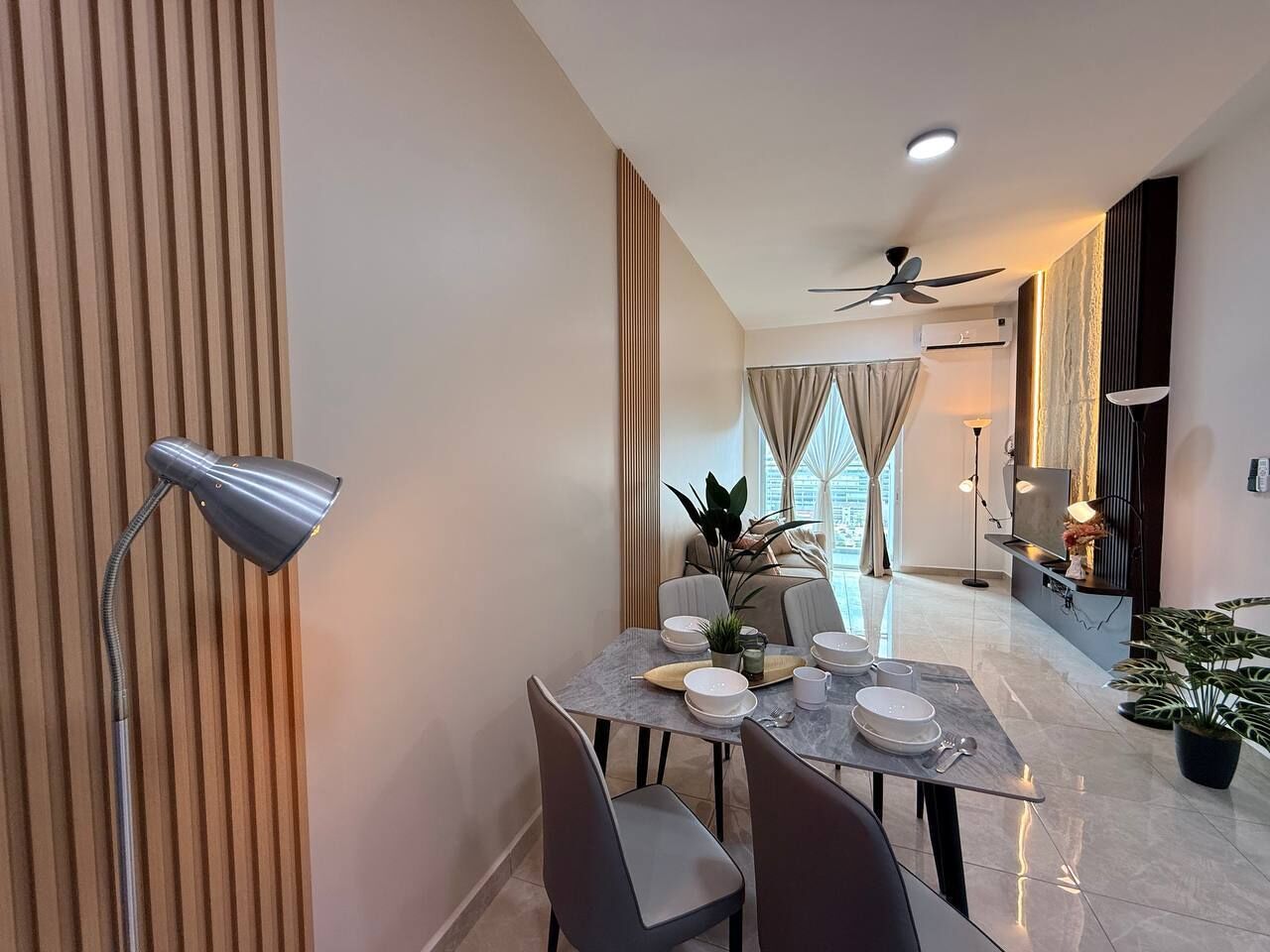Un espace repas moderne avec une table dressée pour quatre personnes, un lampadaire et un ventilateur de plafond.