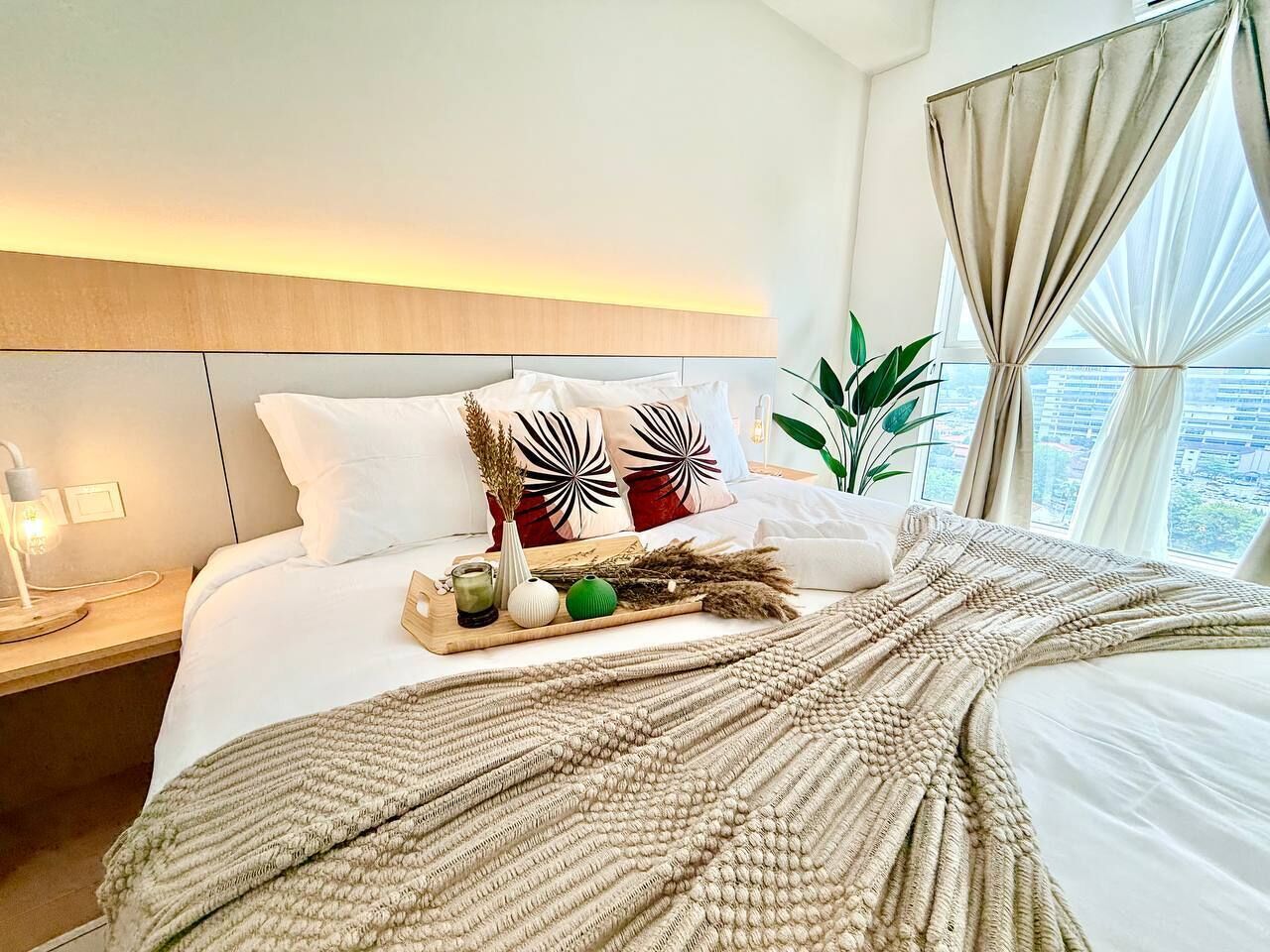 A hotel room with a bed, bedside table, and a window with curtains.