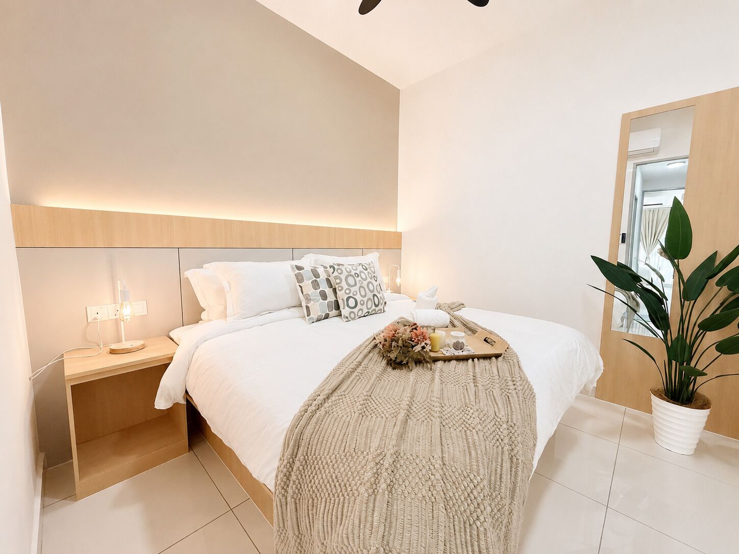 A modern bedroom with a bed, bedside table, lamp, and a potted plant.