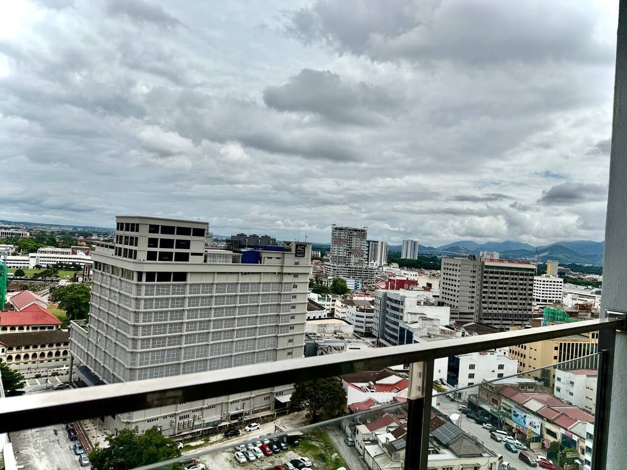 A cityscape with various buildings, including a prominent multi-story building with a grid-like facade and a smaller building with a red roof.
