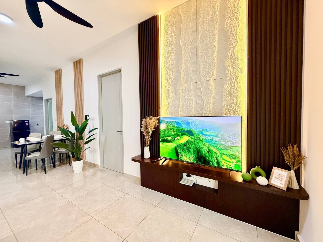 Een moderne woonkamer met een flatscreen televisie, een eethoek en een keuken op de achtergrond.