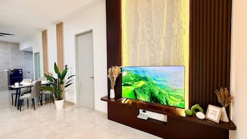 Uma sala de estar moderna com televisão de tela plana, um espaço de jantar e uma cozinha ao fundo.