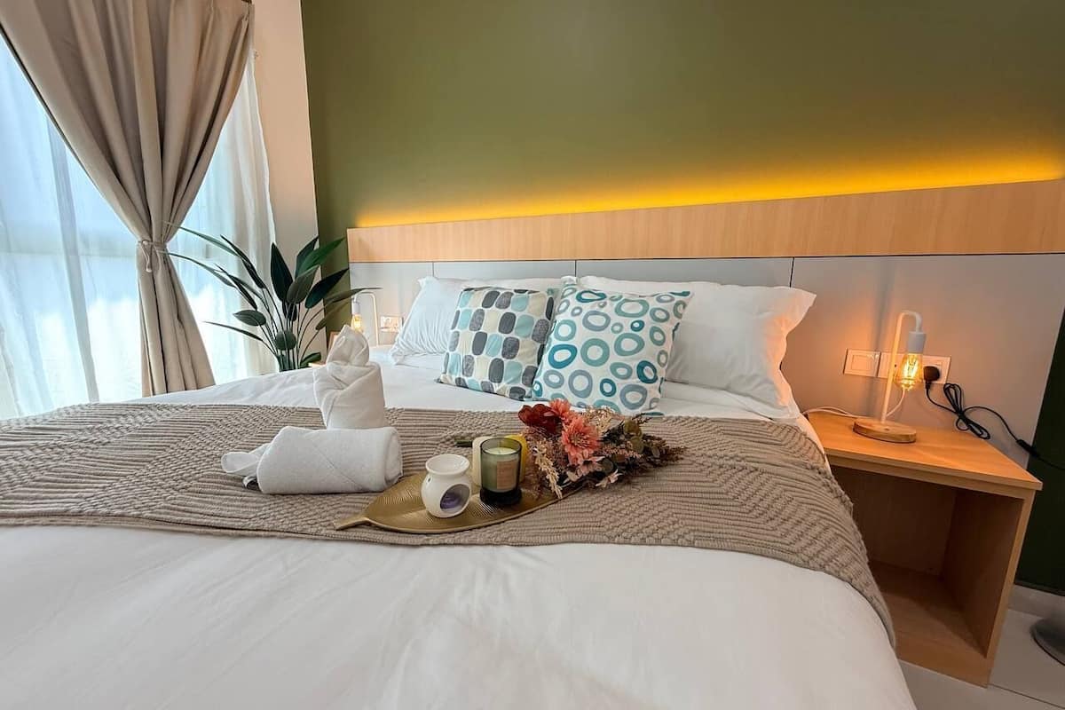 A neatly made bed with a bedside table, a lamp, and a decorative tray with a candle and flowers.