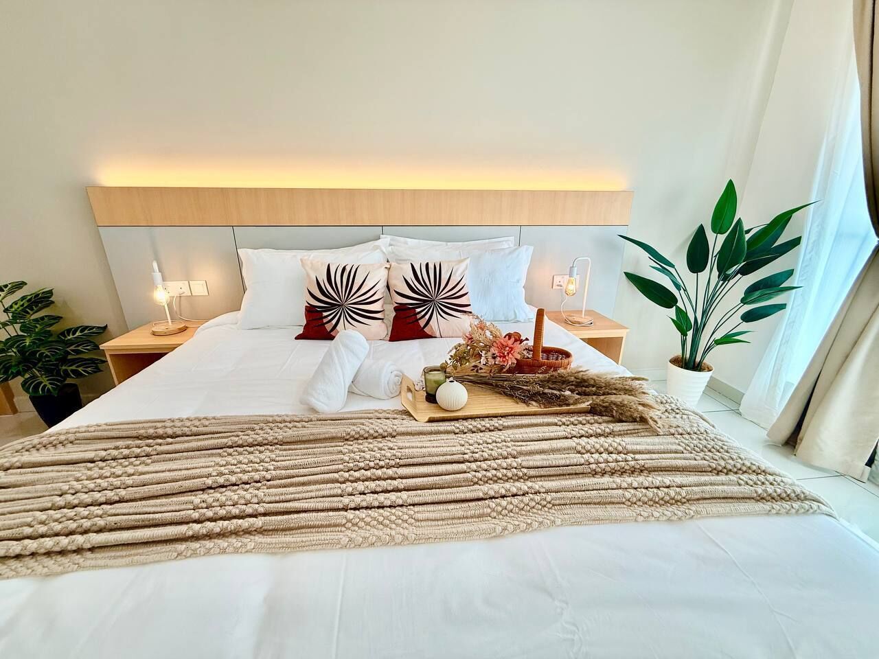 A neatly made bed with a decorative headboard, a bedside table with a lamp, and a potted plant.