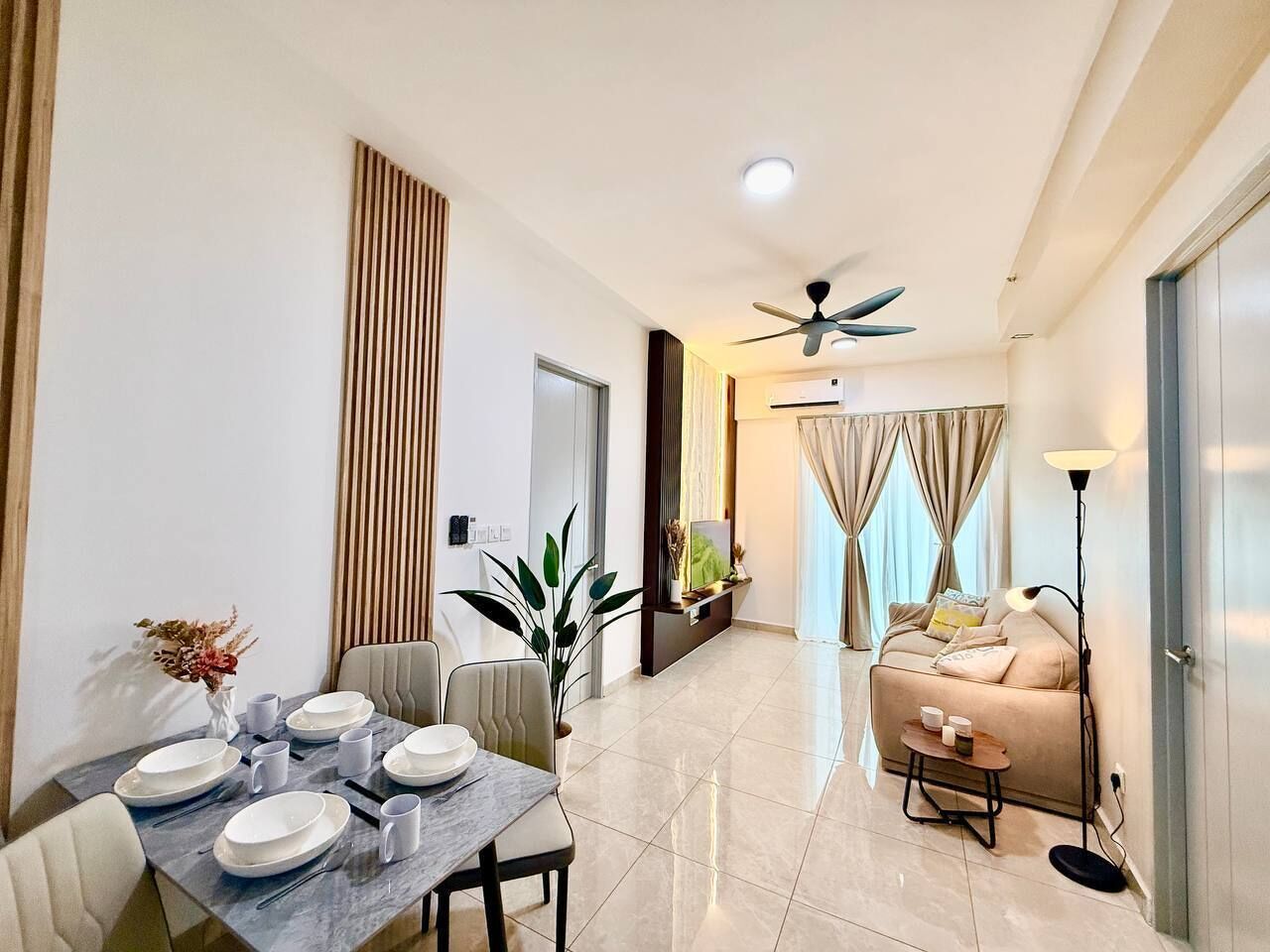 A modern living room with a sofa, a dining table set for four, a ceiling fan, and a large window with curtains.