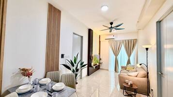 A modern living room with a sofa, a dining table set for four, a ceiling fan, and a large window with curtains.