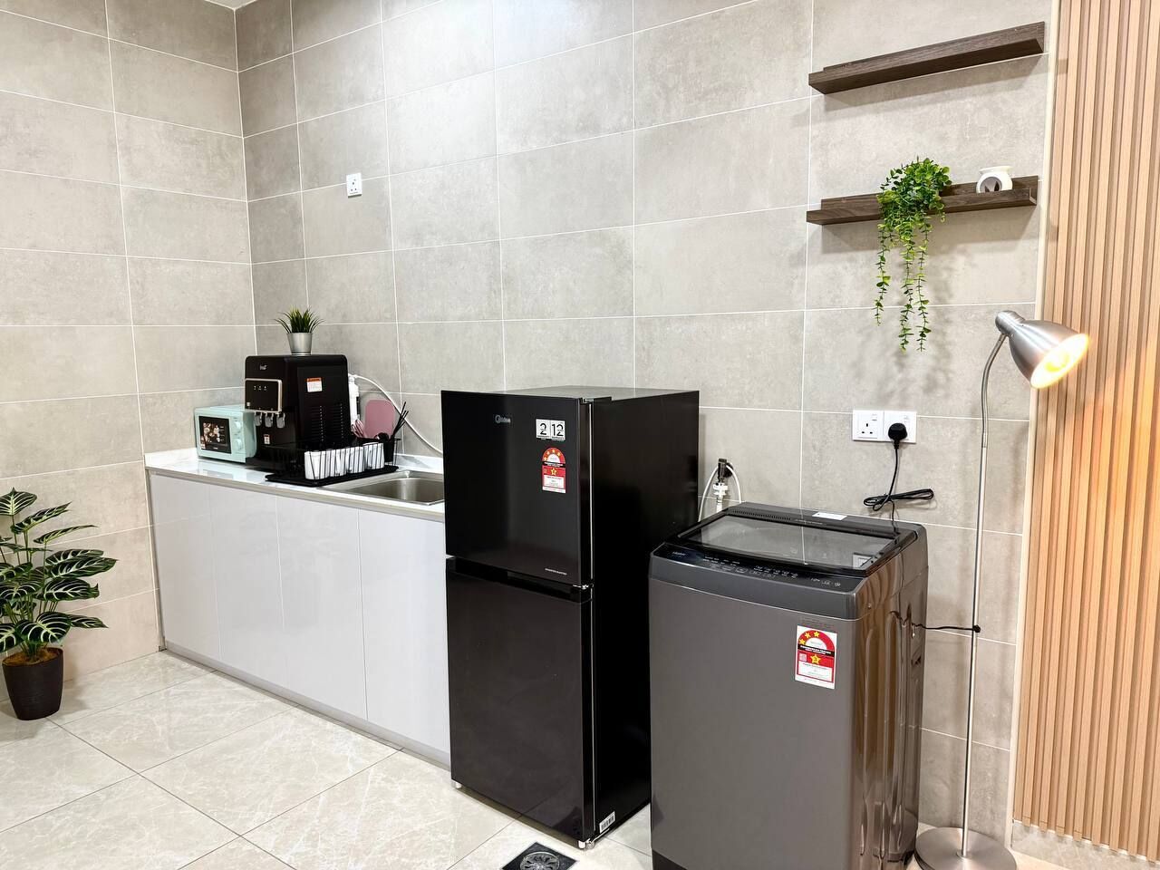 A kitchen with a refrigerator, a microwave, a sink, and a countertop with a plant.