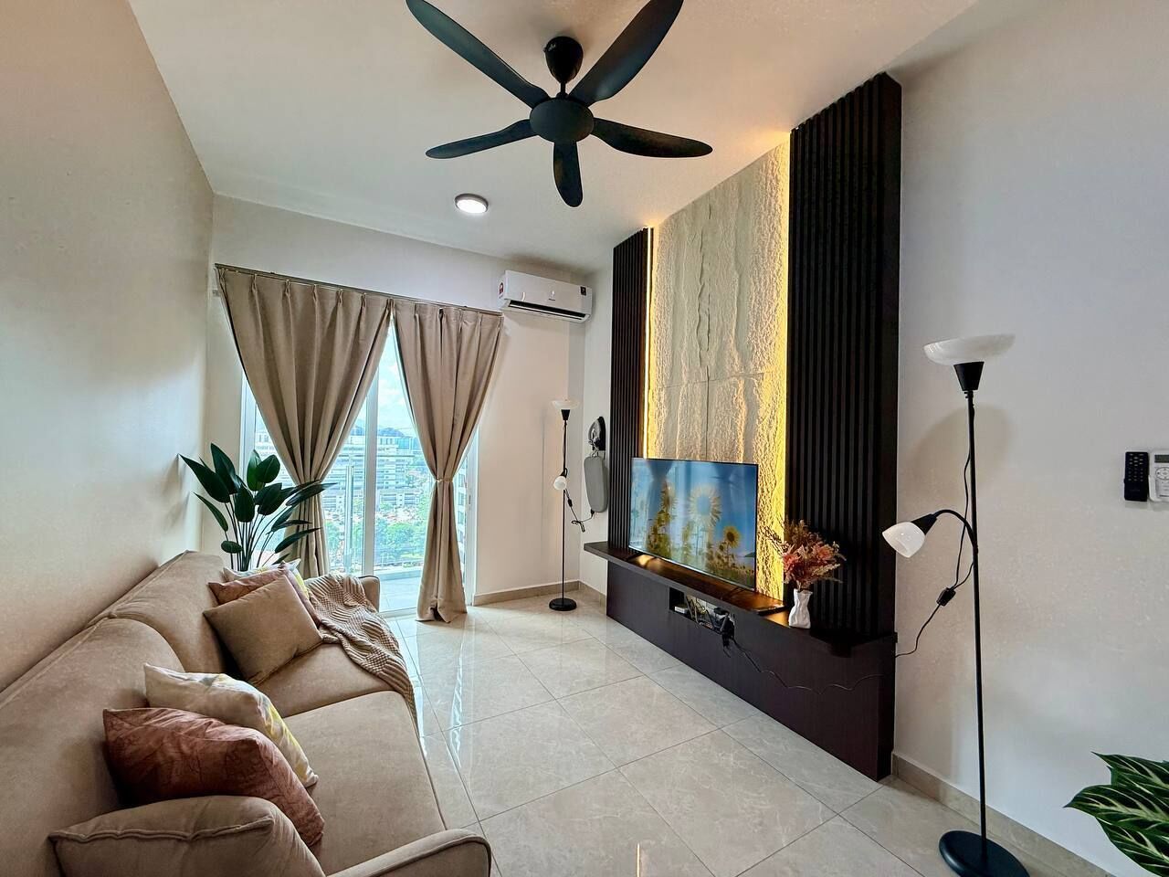 Una sala de estar moderna con sofá, televisión, ventilador de techo y ventanas amplias.