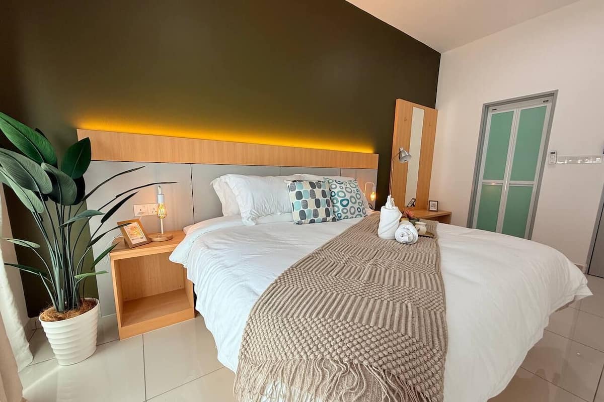 A hotel room with a bed, bedside table, lamp, potted plant, and a door.