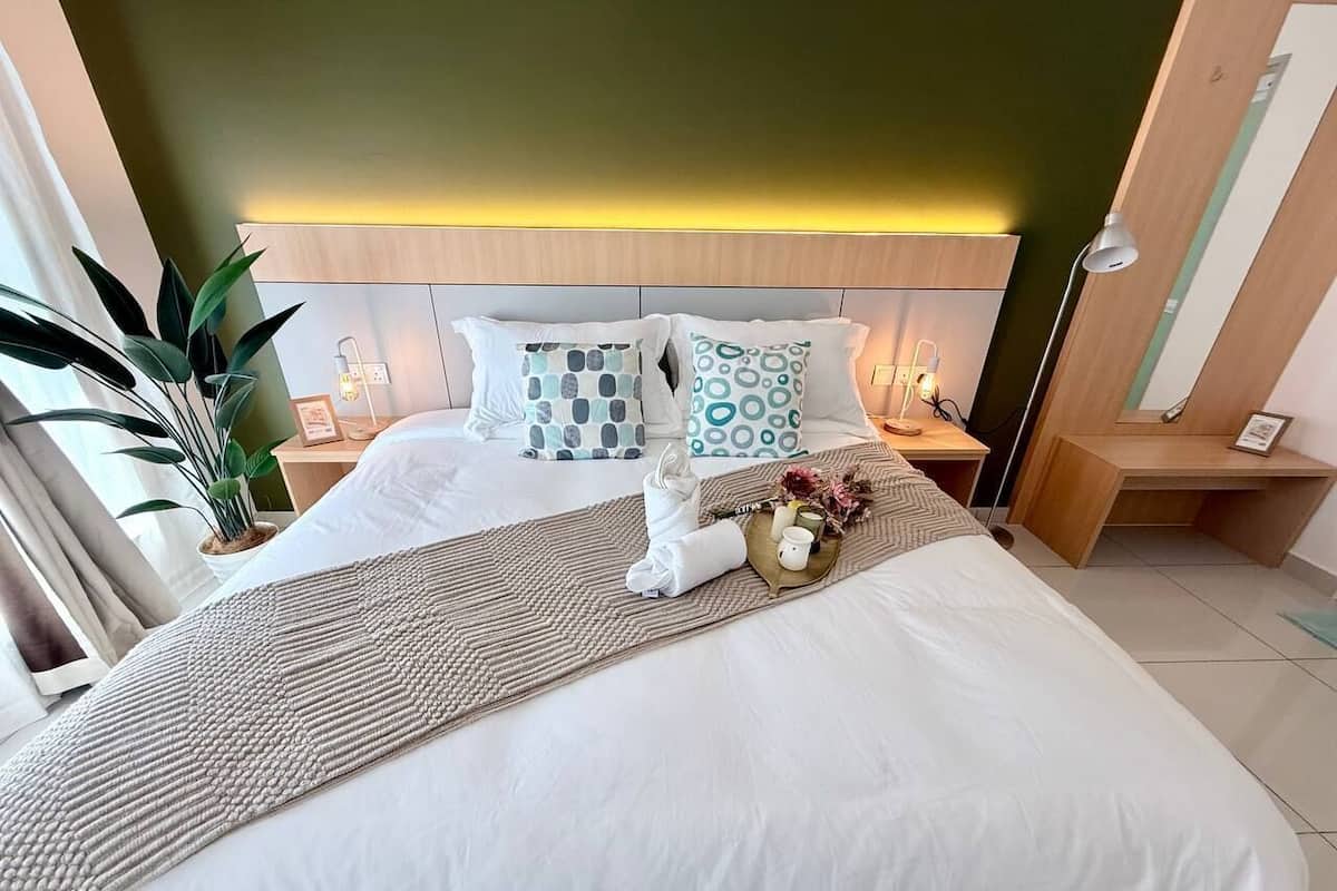A hotel room with a bed, bedside tables, a nightstand, a lamp, and a potted plant.