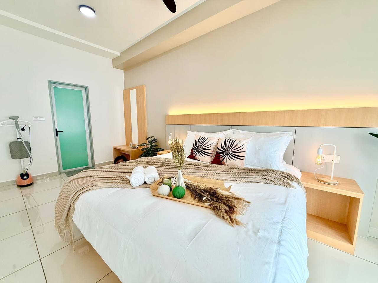 Une chambre d’hôtel moderne avec un grand lit, des tables de chevet, une porte verte et un lampadaire.