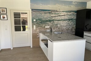 Eine Küche mit einer Granitarbeitsplatte, weißen Schränken, einer integrierten Spüle und einem Wandgemälde mit Strandmotiv.