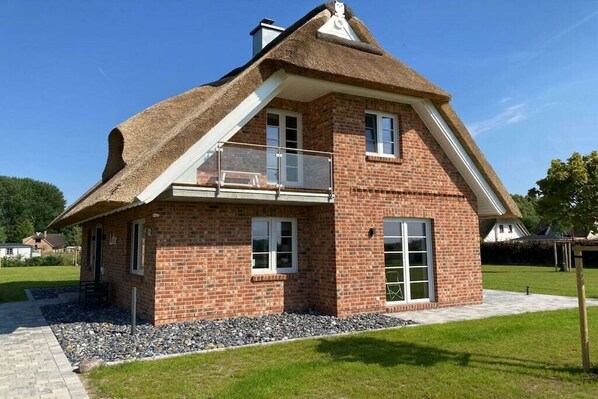 Ein zweistöckiges Haus mit Ziegelaußenwand, einem Strohdach und einem Balkon.