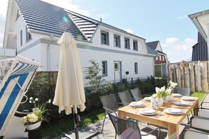 Ein Essbereich im Freien mit einem Tisch für vier Personen, umgeben von Stühlen, einem großen Sonnenschirm und Topfpflanzen.