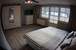Ein Schlafzimmer mit Bett, Kleiderschrank, Schminktisch, Fenster und Deckenventilator.