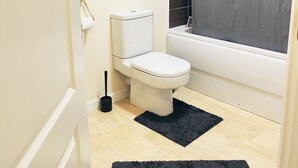 Et badeværelse med toilet, badekar, bruseforhæng og en sort måtte.