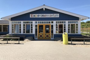 Ein Gebäude mit der Aufschrift 'Experimentarium', einem großen Eingang, Fenstern und einem gelben Mülleimer.