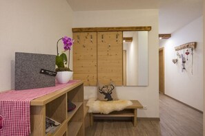 A room with a wooden wardrobe, a small bench with a fur throw, a potted plant, and a wall-mounted mirror. - Holiday apartment with 2 bedrooms (Hippach)