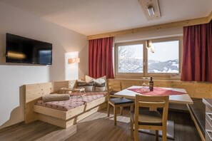 A cozy room with a wooden bed, a dining table, chairs, a TV, and a window with a view of snow-covered mountains. - Holiday apartment with 2 bedrooms (Hippach)