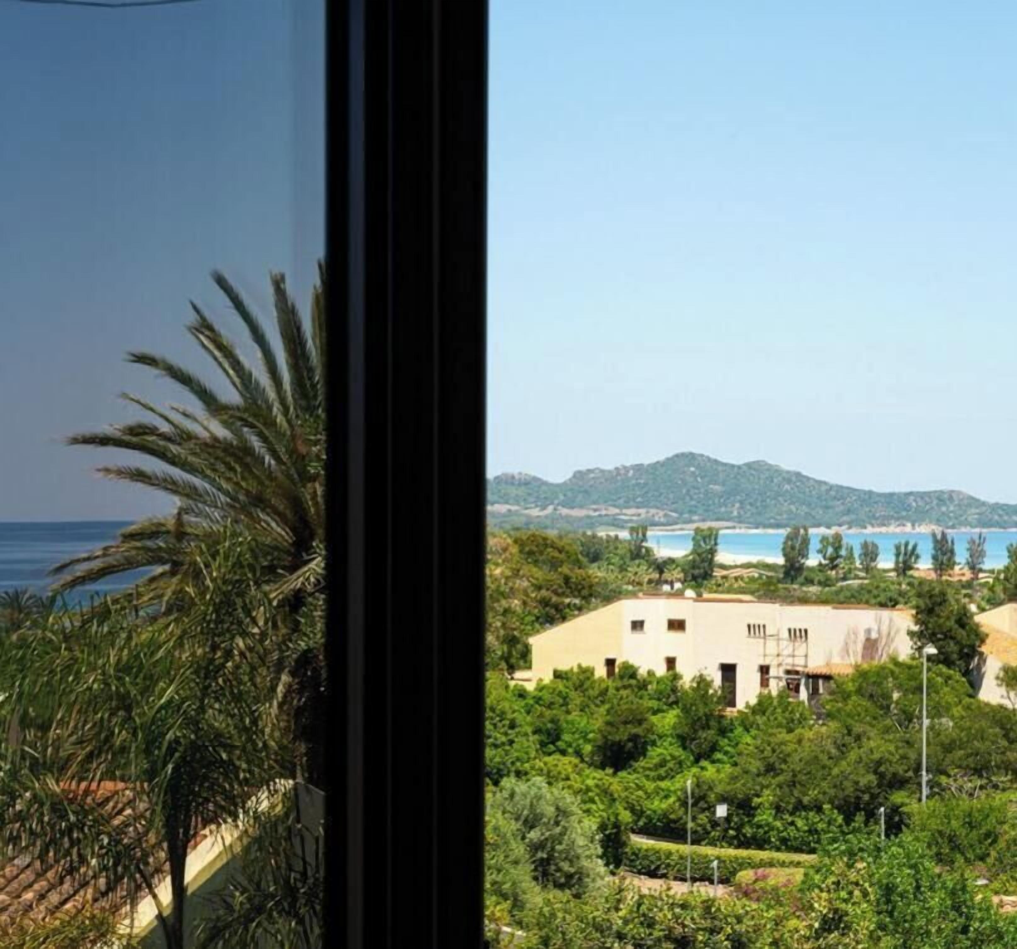A view from a window overlooking a coastal area with a building, greenery, and a clear sky.