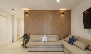 A modern living room with a sectional sofa, a wooden accent wall, and a small side table with a plant. - Villa Reya - Costa Rei Family  Retreat (Costa Rei)