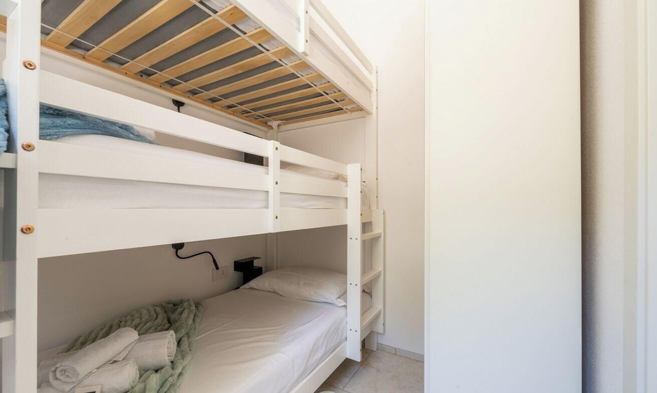 A bunk bed room with a wooden ceiling, a white wall, and a small bedside table.