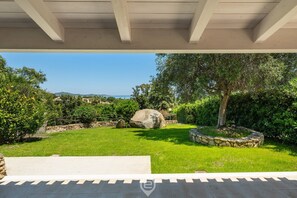 A covered outdoor area with a stone bench, a large rock, and a well-maintained lawn. - Villa Reya - Costa Rei Family  Retreat (Costa Rei)