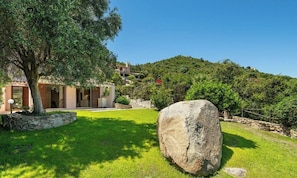 A modern villa with a stone facade, a large rock in the foreground, and a lush green hill in the background. - Villa Reya - Costa Rei Family  Retreat (Costa Rei)