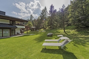 Ein modernes Haus mit gepflegtem Rasen, Sitzgelegenheiten im Freien und einem bewaldeten Hintergrund.