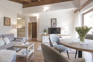 Ein Wohnzimmer mit Sofa, Couchtisch, Fernseher und Essbereich mit Stühlen sowie einem Blumenstrauß.