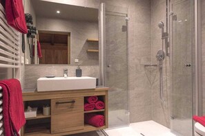 A modern bathroom with a glass shower enclosure, a wooden vanity with a sink, and a mirror above it. - 2-room apartment WALDE in Haus Wildsee (Seefeld in Tirol)