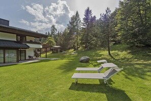 Una casa moderna con un patio, sillas de descanso y zona boscosa.