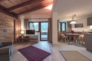 Ein modernes Wohnzimmer mit Fernseher, einer Couch und einem Essbereich mit Stühlen und einem Tisch.
