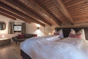 Un dormitorio con techo de madera, una cama con ropa de cama blanca, una mesita de noche, una lámpara y un ventanal con cortinas.