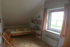 Habitació petita amb un llit individual, una finestra, un radiador i una cadira de fusta.