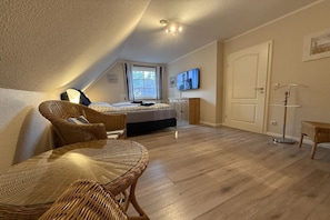 Ein Schlafzimmer mit Bett, Sessel, Tisch, Fernseher und Tür.