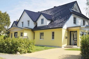 Ein zweistöckiges Gebäude mit gelber Fassade und dunklem Dach, umgeben von Grünflächen.