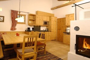 Eine gemütliche Küche mit Holzschränken, einem Esstisch mit Stühlen, einer Mikrowelle und einem Kamin.