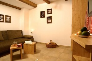 Ein gemütliches Wohnzimmer mit einer Couch, einem kleinen Tisch mit einem Glasbehälter, einem Korb und einer Holzauslage mit einer Obstschale.