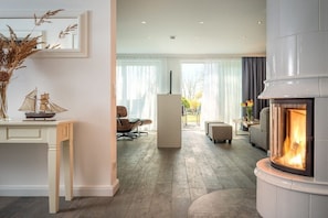A modern living room with a fireplace, a dining area, and a view of the outdoors. - Pilot houses Rügen - Luxury Villa 2 (Breege)