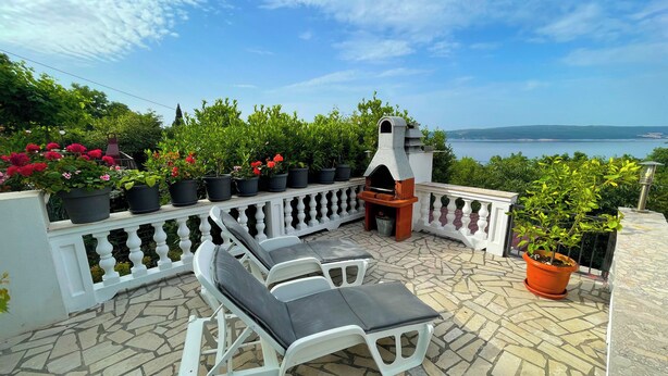 Une terrasse avec des meubles d’extérieur, un barbecue, des plantes en pot et une vue sur la mer.