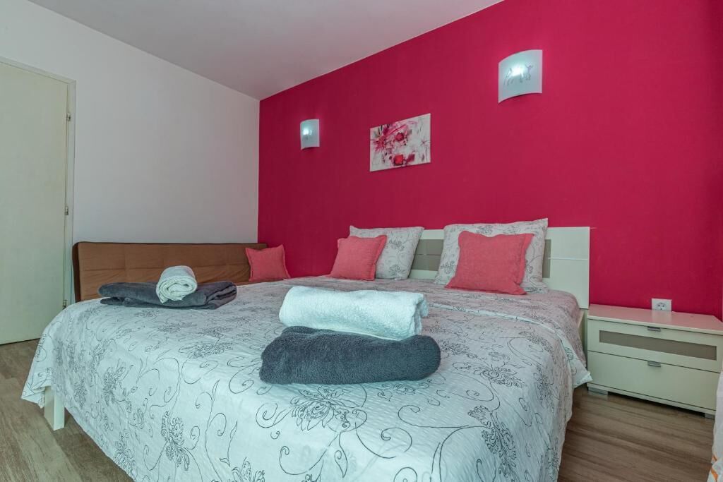 Une chambre à coucher avec un lit, des oreillers, une table de chevet et un mur muni d’un luminaire.