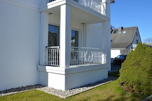 Ein weißes Gebäude mit Balkon, kleinem Garten und einem Nachbarhaus.
