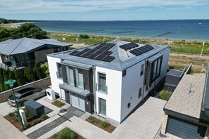 Ein modernes, zweistöckiges Haus mit Solaranlage auf dem Dach, einer Garage und Blick auf das Meer.