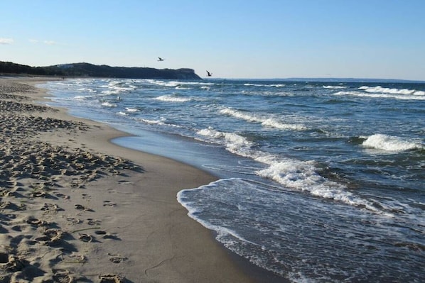 Ein Strand mit Wellen, einem sandigen Ufer und einer entfernten Küstenlinie.