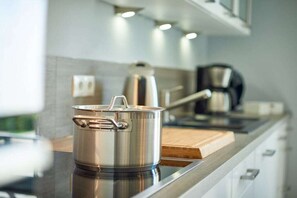 Ein Edelstahlkochtopf auf einer Küchenarbeitsplatte mit einem Holzschnittbrett, einer Kaffeemaschine und einem Wasserkocher im Hintergrund.
