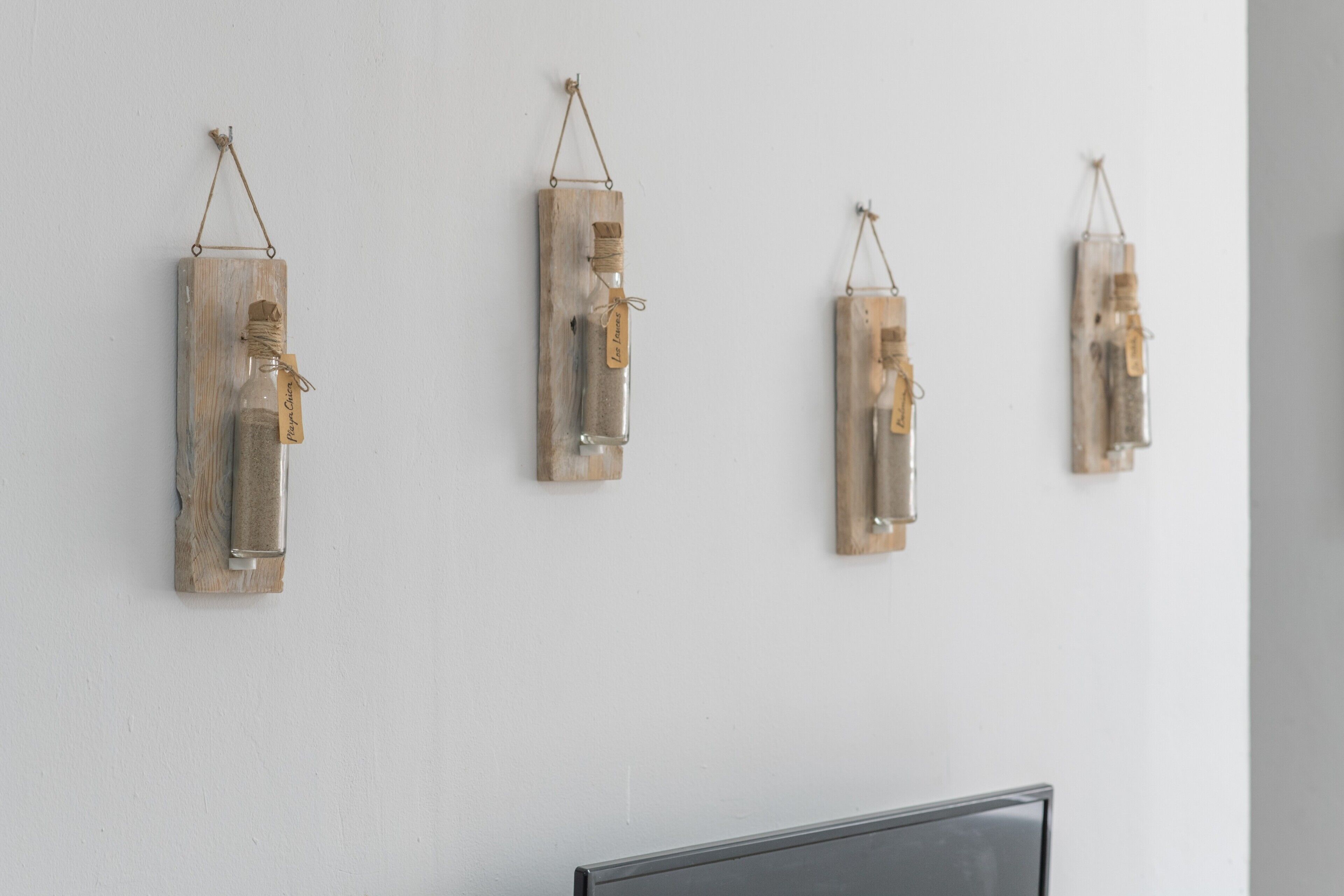 Quatre bouteilles décoratives, fixées au mur et dotées d’étiquettes, disposées en rangée sur un mur uni.